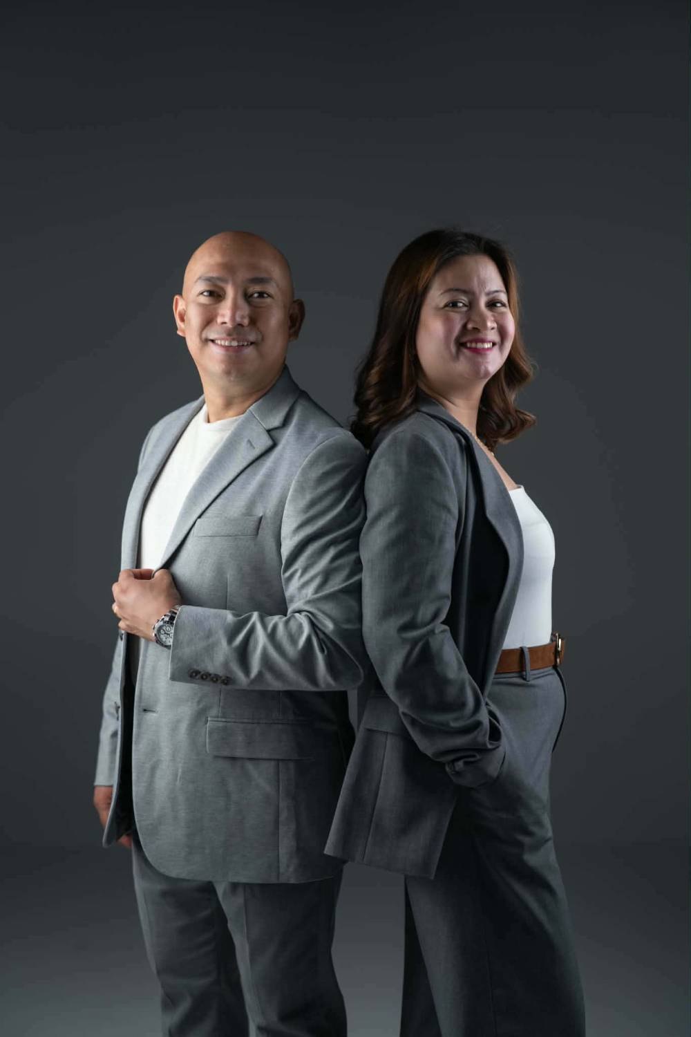 Jover Loberial, BSN, RN and Charmaine Loberial, BSN, RN standing back to back in grey suits